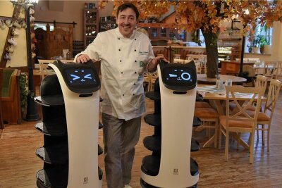 Im Landhotel Zum grünen Baum in Taltitz servieren jetzt Roboter - Silvio Kuhnert mit seinen neuen Helfern: Zwei Roboter werden künftig die Gäste in seinem Restaurant bedienen. Die Geräte mit Katzengesicht wurden auf die Namen Bella und Robby getauft. Foto: Christian Schubert