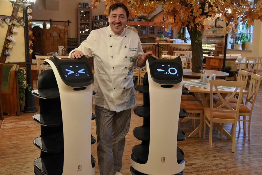 Silvio Kuhnert mit seinen neuen Helfern: Zwei Roboter werden künftig die Gäste in seinem Restaurant bedienen. Die Geräte mit Katzengesicht wurden auf die Namen Bella und Robby getauft. Foto: Christian Schubert