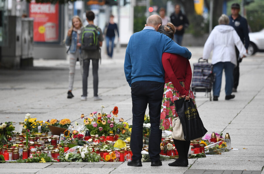 Passanten stehen am Tatort an der Brückenstraße, an dem zahlreiche Blumen und Kerzen niedergelegt wurden. 