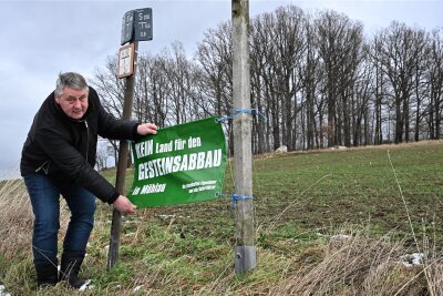Jahrzehntelanger Rechtsstreit in Mühlau beendet: Kein Gesteinsabbau auf dem Windberg - Bürgermeister Frank Rüger zeigt das Plakat „Kein Land für den Gesteinsabbau in Mühlau“. Der jahrzehntelange Protest hatte jetzt Erfolg.