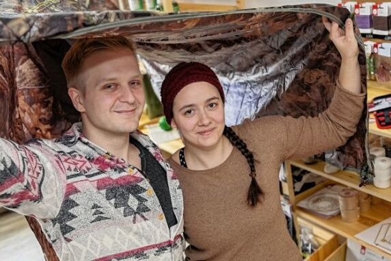 Junges Paar öffnet Outdoor-Laden - Patrick Leonhardt und Laura Knape mit dem Tarp, das man zum Übernachten im Wald aufspannen kann.