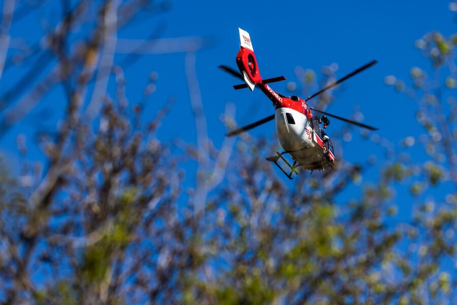 Kind fällt in Felsspalte in Sächsischer Schweiz - Ein Helikopter der DRF Luftrettung schwebt am Himmel über einem Waldstück.