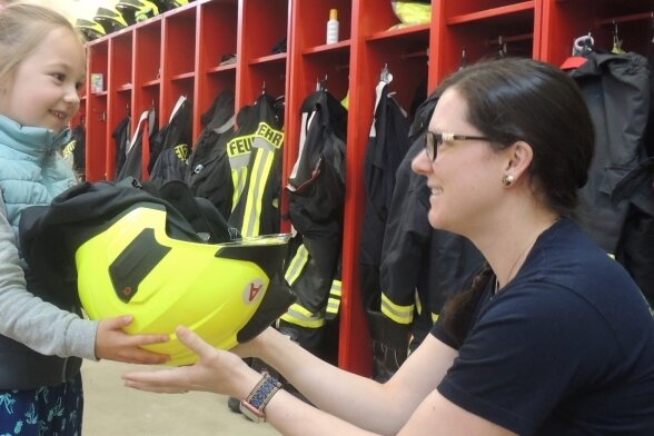 Feuerwehrfrau Karin Werner zeigt Emma Clemens, wie schwer der Schutzhelm ist. Die Gäste aus der Kinderstube Leubnitz waren begeistert.