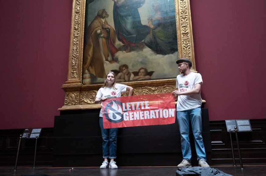 Klebeaktion von Klimaaktivisten in der Gemäldegalerie Alte Meister - Zwei Umweltaktivisten der Gruppe "Letzte Generation" stehen mit einem Banner in der Gemäldegalerie Alte Meister an dem Gemälde "Sixtinische Madonna" von Raffael.