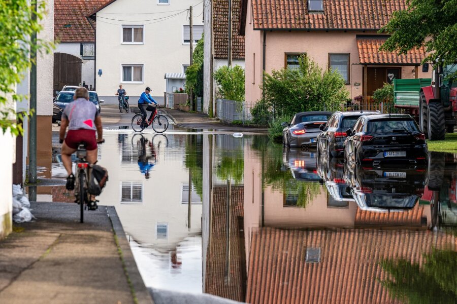 Klimawandel verschlimmerte Hochwasser - Radler fahren durch eine überflutete Straße. Im Bereich der Gemeinde Baar-Ebenhausen war ein Damm an zwei Stellen geborsten.