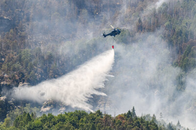 Ein Hubschrauber der Bundespolizei fliegt mit einem Löschwasser-Außenlastbehälter um einen Waldbrand im Nationalpark Sächsische Schweiz zu löschen.