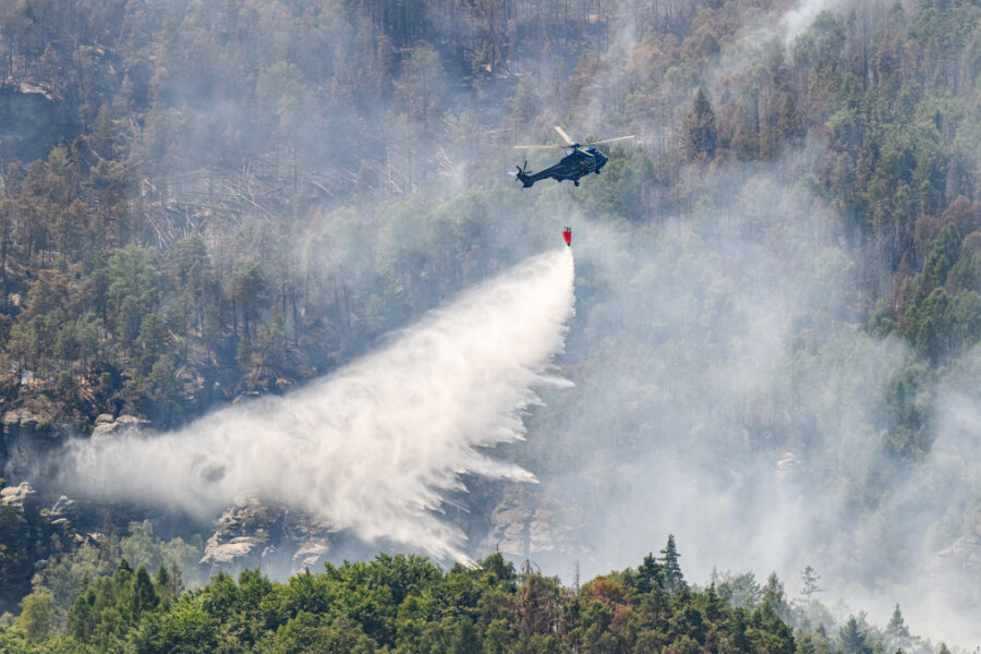 Ein Hubschrauber der Bundespolizei fliegt mit einem Löschwasser-Außenlastbehälter um einen Waldbrand im Nationalpark Sächsische Schweiz zu löschen.