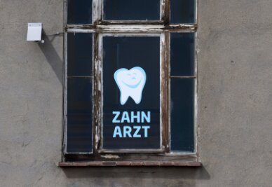 Landeszahnärztekammer fördert Berufseinstige - Zahnarzt steht an einem Fenster eines Hauses, in dem sich eine Zahnarztpraxis befindet, geschrieben.