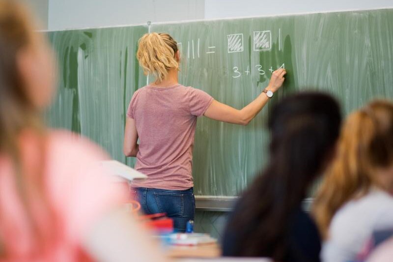           Eine junge Lehrerin schreibt im Unterricht an eine Schultafel.