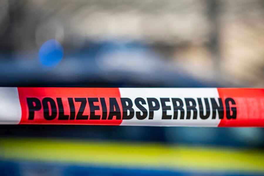 Leiche in Bischofswerda gefunden - Polizei ermittelt - Ein Absperrband mit der Aufschrift "Polizeiabsperrung" ist vor einem Polizeiwagen aufgespannt.