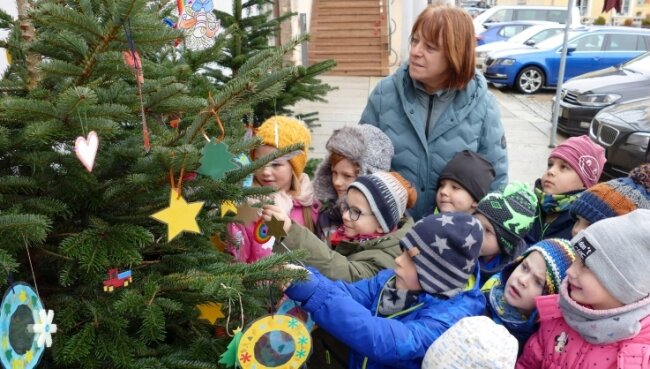 Zusammen mit Erzieherin Ramona Böhmer hängen Kinder der Kita Pfiffikus gebastelten Weihnachtsbaumschmuck vor dem Rathaus auf. 