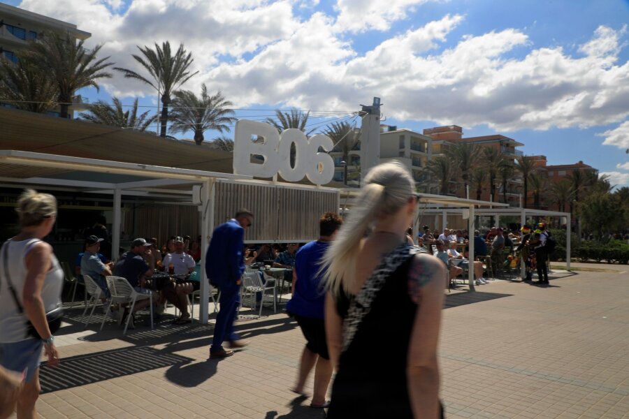 Mallorcas Polizei vertreibt deutsche Fans mit Platzpatronen - Menschen spazieren an einem sonnigen Tag am Ballermann 6 vorbei.