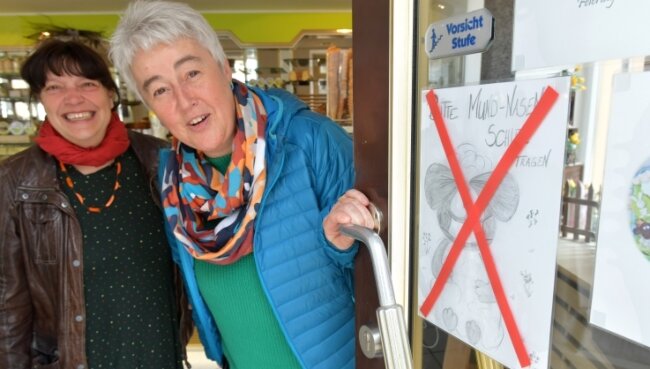 Maskenpflicht: Kunden entscheiden selbst - Lustiges Hinweisschild für das Ende der Maskenpflicht in Geschäften an der Eingangstür Cafè Andelt am Untermarkt in Freiberg. Hier hatte Inhaber Daniel Wolf das von seiner Frau Peggy gemalte Schild angebracht. Silke Sohr und Grit Trinks freuten sich.