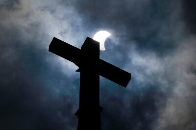 Millionen Menschen sehen totale Sonnenfinsternis - Wolken lösen sich auf und geben über dem Kreuz eines Kirchturms in Manor (Texas) den Blick auf die beginnende Sonnenfinsternis frei.