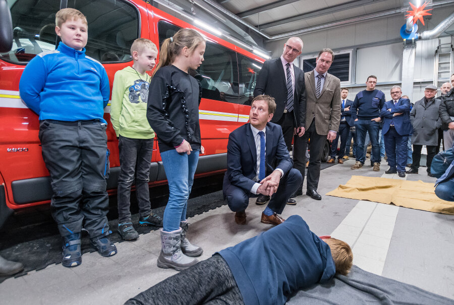 Ministerpräsident besucht Feuerwehr - Im Gerätehaus der Freiwilligen Feuerwehr Kühnhaide ließ sich Ministerpräsident Michael Kretschmer (4.v.l.) von Nomi Lorenz (3.v.l.) von der Jugendfeuerwehr zeigen, wie die stabile Seitenlage funktioniert.