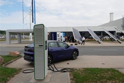 Mit ausgedienten E-Auto-Batterien: VW nimmt Ladepark in Zwickau in Betrieb - Der Schnellladepark im VW-Werk Mosel nebst Solar- und Windkraftanlagen. Im Vordergrund eine von vier Ladesäulen. Hinter dem Fahrzeug ist auf der anderen Straßenseite der Power Storage Container zu sehen. 