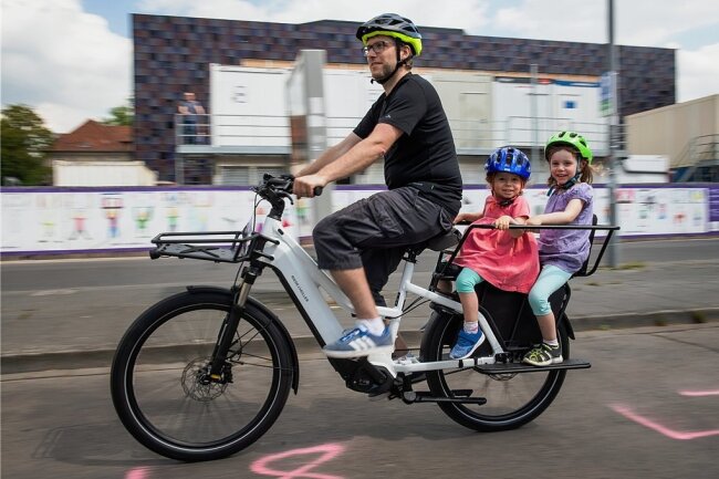 Papa hat das coolste Fahrrad: Auf dem Heckträger dieses E-Cargobikes fahren zwei Kinder mit.