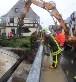 Nach der Flut beginnt das Aufräumen - In Bockau wurde am Kapellenbach eine Gasleitung destabilisiert. Feuerwehrleute befestigten sie vorerst an einem Stahlträger.
