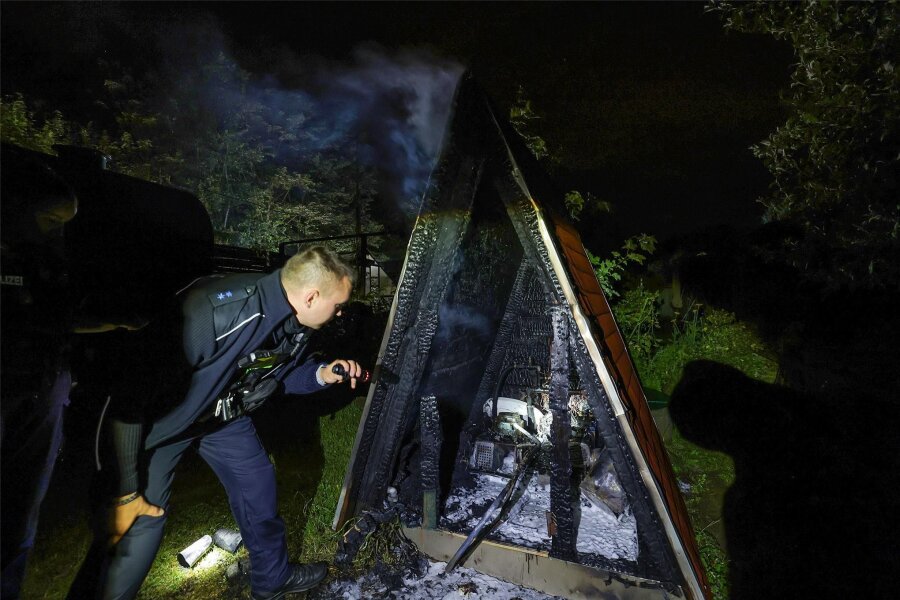 Nach Explosion in Zwickau: Pumpenhaus in Kleingartenanlage in Cainsdorf abgebrannt - Ein Polizist inspiziert das ausgebrannte Pumpenhaus in der Cainsdorfer Gartenanlage.