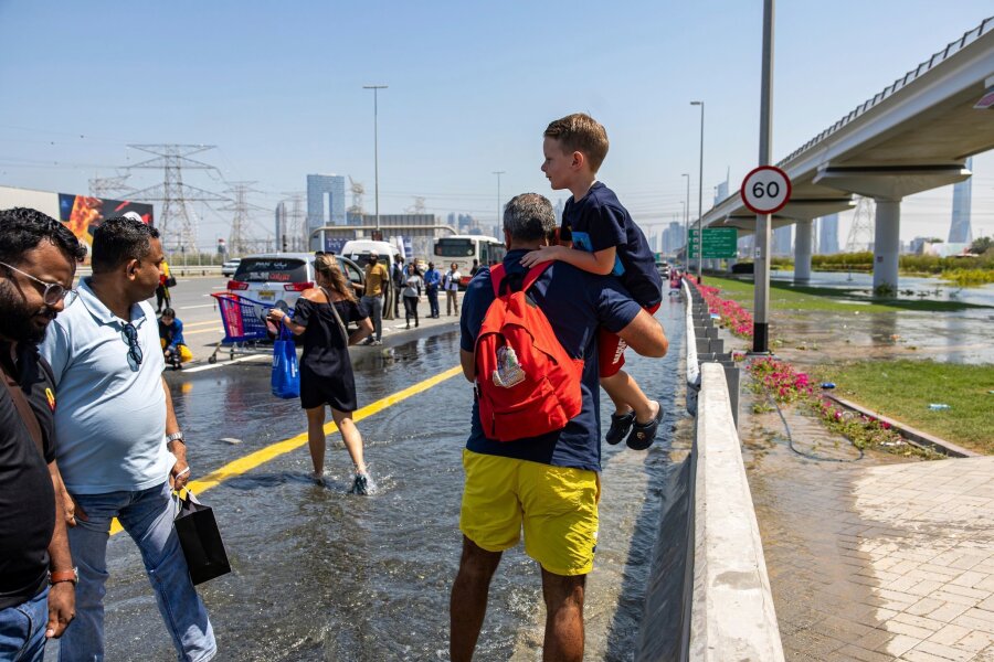 Nach Unwetter in Dubai weiter Störungen am Flughafen - Ein Mann trägt ein Kind durch das von starkem Regen verursachte Hochwasser in Dubai.