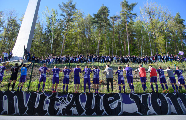 Aues Spieler feiern nach dem Spiel mit Fans, die vor dem Stadion im Wald stehen.