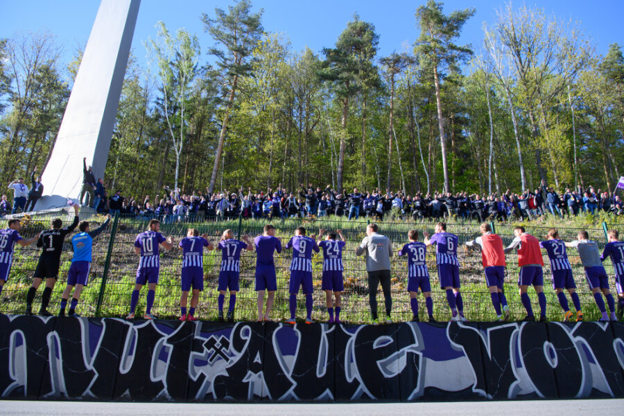 Aues Spieler feiern nach dem Spiel mit Fans, die vor dem Stadion im Wald stehen.