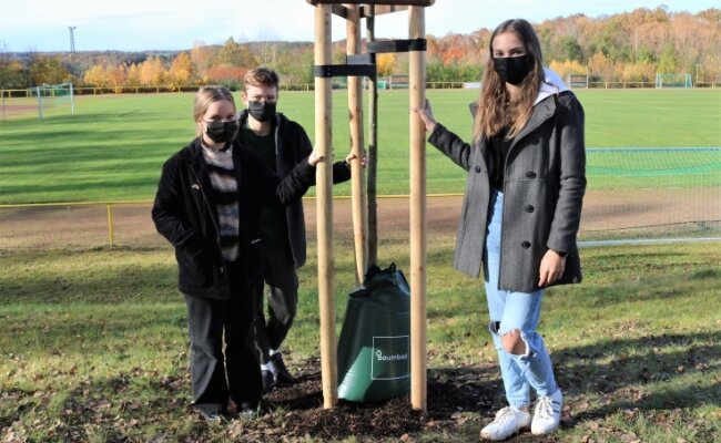 Julienne Heidrich, Philippe Börner und Lilly Schöne (v. l.) von der Klimagruppe der Oberschule Niederwiesa sind froh, dass auf dem Sportplatz zehn neue Bäume gepflanzt wurden. 