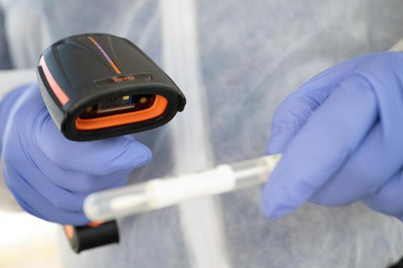            Ein Arzt in Schutzkleidung scannt ein Teststäbchen in einer mobilen Corona-Teststation.