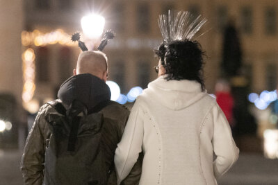 Neues Jahr beginnt in Sachsen eher ruhig - Ein Mann und eine Frau tragen besonderen Kopfschmuck zum Jahreswechsel, während diese in Richtung der Frauenkirche in Dresden laufen.