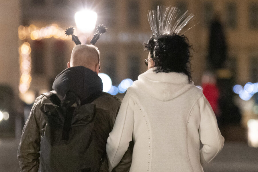 Neues Jahr beginnt in Sachsen eher ruhig - Ein Mann und eine Frau tragen besonderen Kopfschmuck zum Jahreswechsel, während diese in Richtung der Frauenkirche in Dresden laufen.