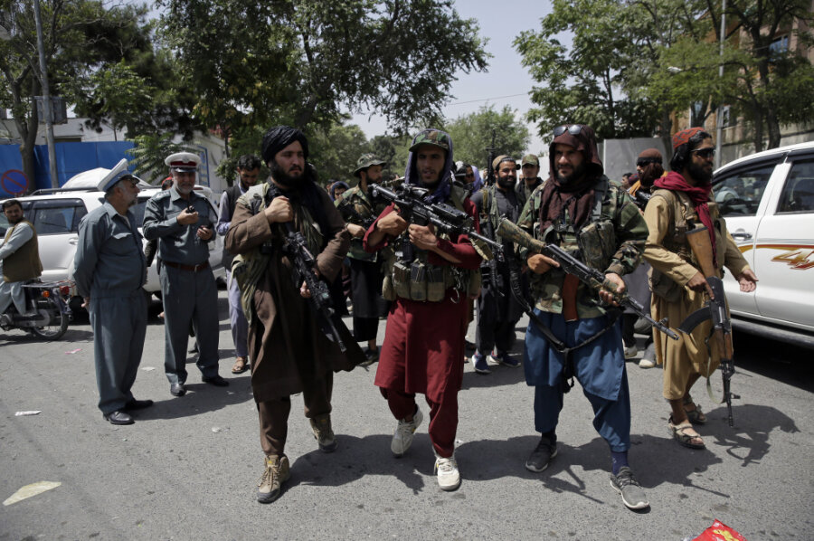 Schwer bewaffnete Taliban-Kämpfer patrouillieren vor zwei Verkehrspolizisten.
