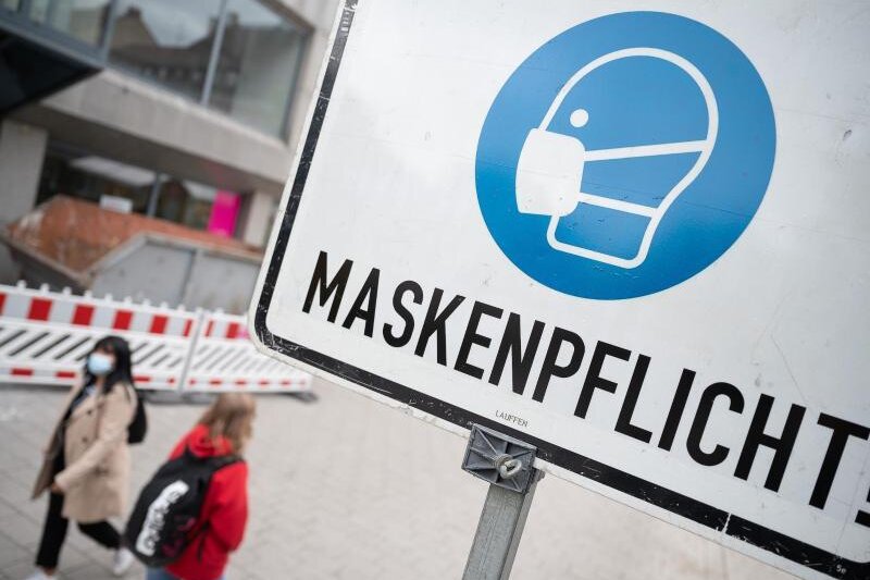            Zwei Passantinnen gehen in einer Fußgängerzone hinter einem Schild vorbei, auf dem «Maskenpflicht» steht.