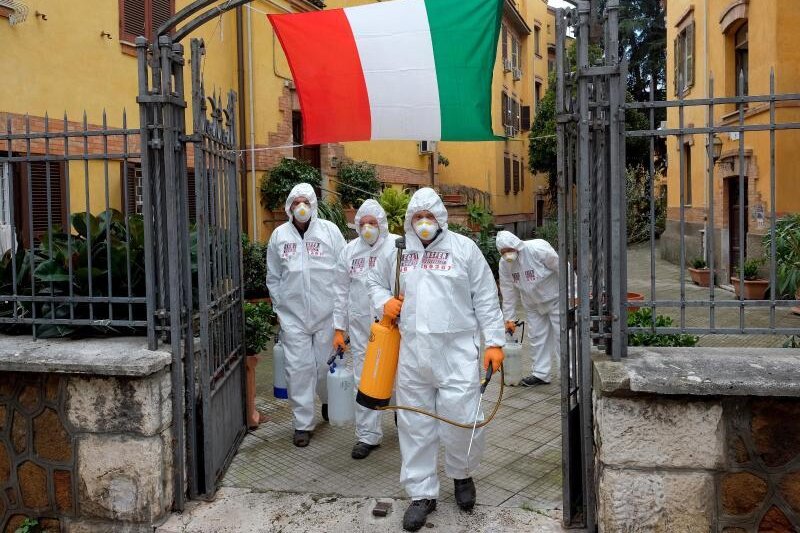            Arbeiter in Schutzkleidung desinfizieren Gehwege in Rom.