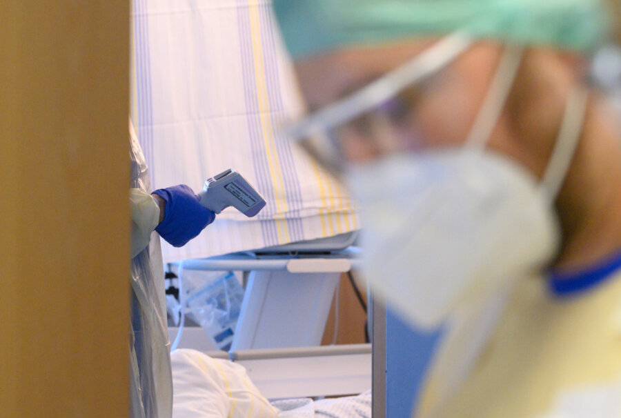 Newsblog Coronavirus - die aktuelle Entwicklung - Ein Pfleger hält in einer Corona-Notaufnahme ein digitales Fiebermessgerät in einem Patientenzimmer in der Hand, während ein zweiter Pfleger vor der Tür steht.