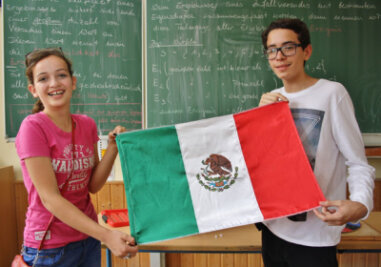 Niederwiesaer feiern Jubiläum und bekommen Besuch aus Mexiko - Anna Biro (l.)  und Rodrigo Sumohano zeigen in  einem Klassenzimmer der Oberschule Niederwiesa die mexikanische Flagge.