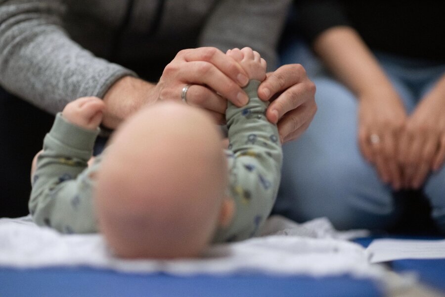 Nur noch knapp jeder Zweite lebt in einer Familie - Ein Vater hält während eines Infant Handling Kurses die Füße seines Kindes, während die Mutter daneben sitzt.