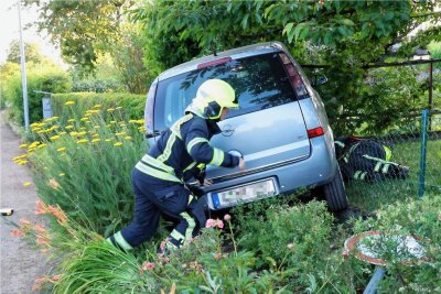 Opel verunglückt in Chemnitzer Gartenanlage – Feuerwehr muss Fahrer befreien - Einsatz in einem Kleingartenverein in Chemnitz-Ebersdorf: Feuerwehrleute kümmern sich um das verunglückte Auto.