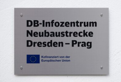 Planung für Eisenbahntunnel im Erzgebirge fast abgeschlossen - Ein Schild mit der Aufschrift „DB-Infozentrum Neubaustrecke Dresden - Prag“ hängt an einem Gebäude.