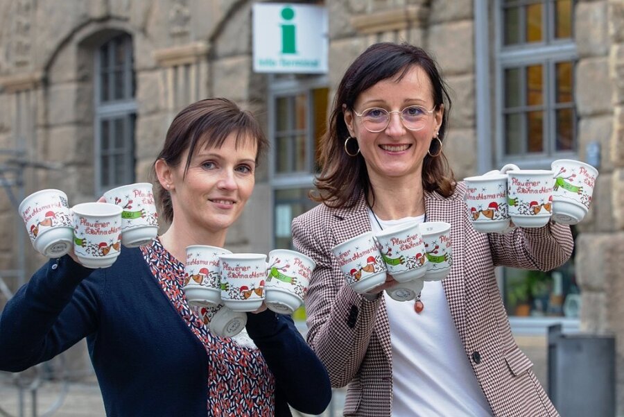 Plauener Glühweintasse 2021 jetzt endlich erhältlich - Kathleen Dentler und Anja Linke (von links) freuen sich, endlich in der Tourist-Information die neue Plauener Glühweintasse verkaufen zu können. 