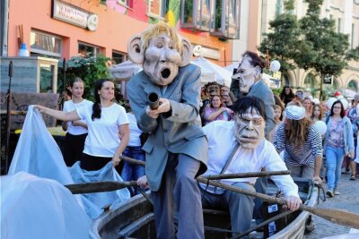 Politische Töne bei der Puppen-Parade in Zwickau - Kapitalismus-Kritik im Puppenkostüm: Drei Gestalten in grauen Anzügen wollen auf einem Boot zu der Wunschinsel schippern, sie mit ihrem Geld vereinnahmen und mit ihrer Gier zerstören. 