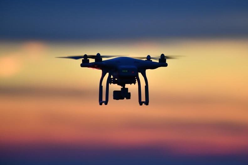            Eine Drohne fliegt bei Sonnenuntergang über eine Wiese.