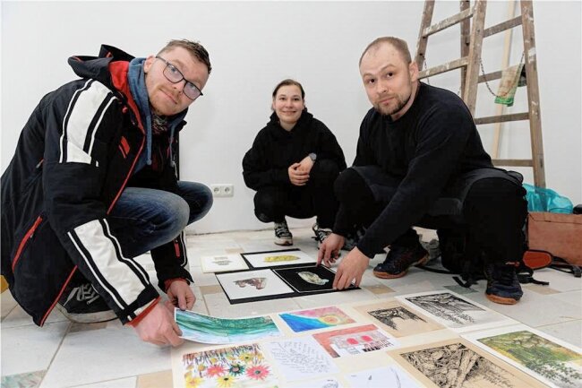 Premiere im Erzgebirge: Annaberger Markt wird zur Leinwand für Straßenkunst - Denis Bremora und Elisa Dietze aus Ehrenfriedersdorf sowie Markus Thierfelder (von links) aus Thum aus dem Zeichenkurs der Alten Brauerei ordnen ihre Bilder für die Schaufensterpräsentation an. 