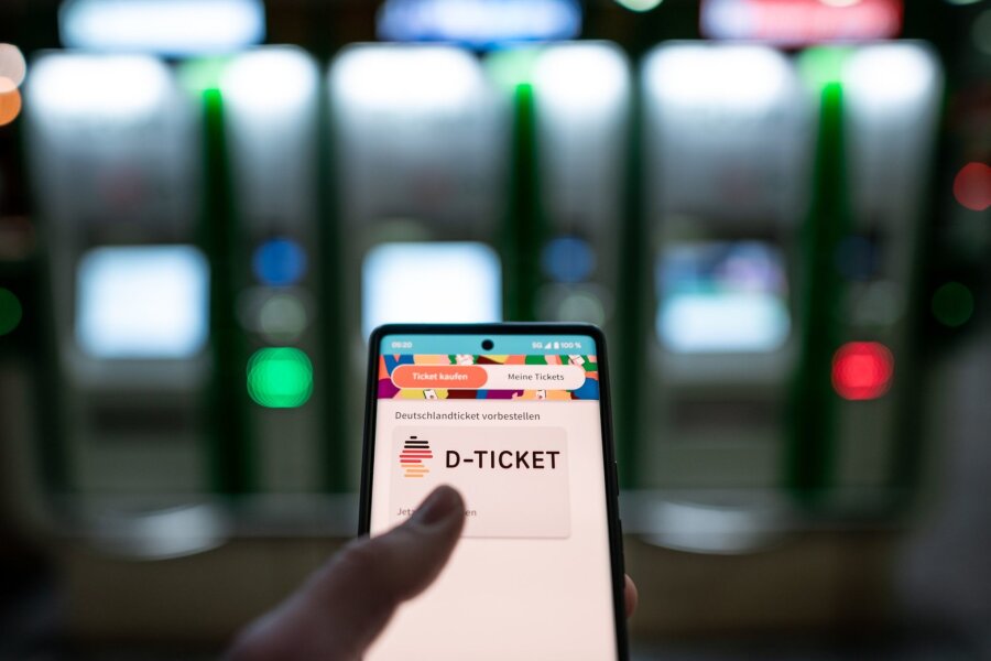 Pro Bahn will Wahloption beim Schüler-Deutschlandticket - Ein Mann hält ein Mobiltelefon, auf dem das „D-Ticket“ gekauft werden kann, vor Ticketautomaten am Hauptbahnhof in der Hand.