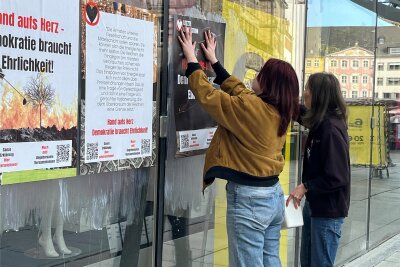 Protestaktion in Chemnitz: Letzte Generation klebt Plakate an Galeria-Kaufhof-Fassade - Mit Tapetenkleister klebten am Samstag zwei Aktivistinnen der Letzten Generation Plakate an die Glasfassade des Galeria-Kaufhof-Gebäudes.