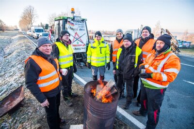 Proteste im Erzgebirge: Wer hinter der Blockade der B 169 in Schneeberg steht - An aufgestellten Feuertonnen wärmen sich die Männer auf, die mit ihren Fahrzeugen auf der B 169 in Schneeberg eine Blockade bilden.