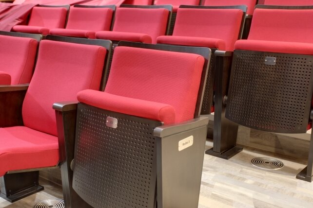 Publikum sitzt auf Stühlen aus Italien - Breitere Sitze und wesentlich mehr Beinfreiheit als vorher.