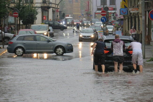 Nach dem Unwetter steckte ein Fahrzeug in den Fluten auf der Auer Bahnhofstraße fest. Fußgänger schoben das Auto aus dem Wasser. 