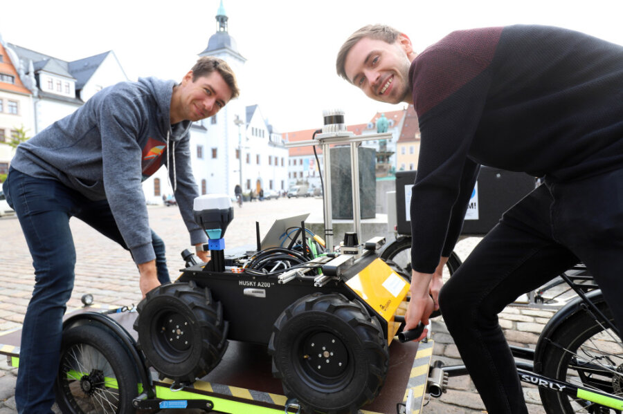 Die wissenschaftlichen Mitarbeiter an der TU Bergakademie Freiberg, Norman Seyffer (l.) und Lorenzo Neumann, heben den Testroboter auf den Obermarkt.