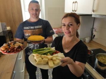 Rumänische Mitarbeiter bei Saxonia sind im neuen Zuhause auf dem Wasserberg angekommen - Elena und Alin Cracana aus Rumänien haben in ihrer Wohnung zu Mittag gekocht. Elena bringt einen gemischten Teller mit Käse zum Tisch, Alin einen Slanina-Wurstteller und Màmàligà-Kuchen. 
