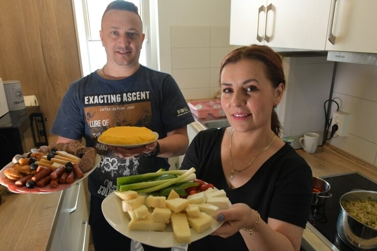Elena und Alin Cracana aus Rumänien haben in ihrer Wohnung zu Mittag gekocht. Elena bringt einen gemischten Teller mit Käse zum Tisch, Alin einen Slanina-Wurstteller und Màmàligà-Kuchen. 